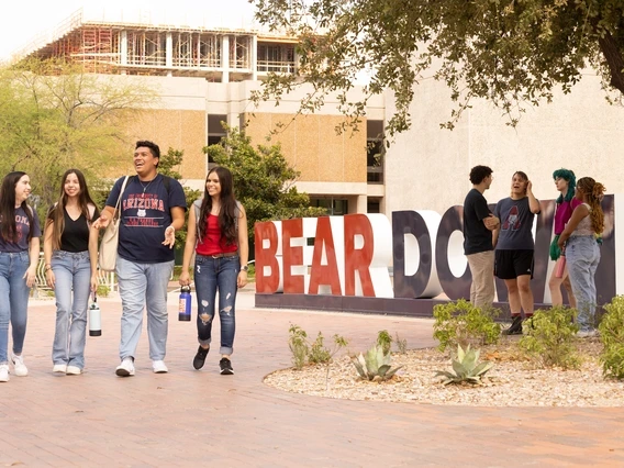 students walking past the U of A main library in front of a large "Bear Down" sign