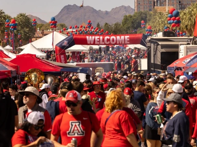 A large crowd of University of Arizona fans fills the University of Arizona Mall during Homecoming festivities, surrounded by red and blue tents, balloons, and a “Welcome” archway with mountains visible in the background.