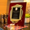 A close-up of a plaque reading "2025 Most Improved Clery Compliance Program, presented to University of Arizona," displayed on a countertop with small decorative items around it.