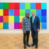 two men standing in front of a work of art depicting people's faces in colored squares