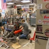Workshop with people assembling a racing vehicle, surrounded by tools and automotive banners.